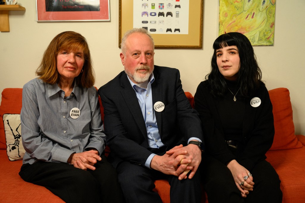 evan's parents sit on a red couch and they're wearing "free evan" badges