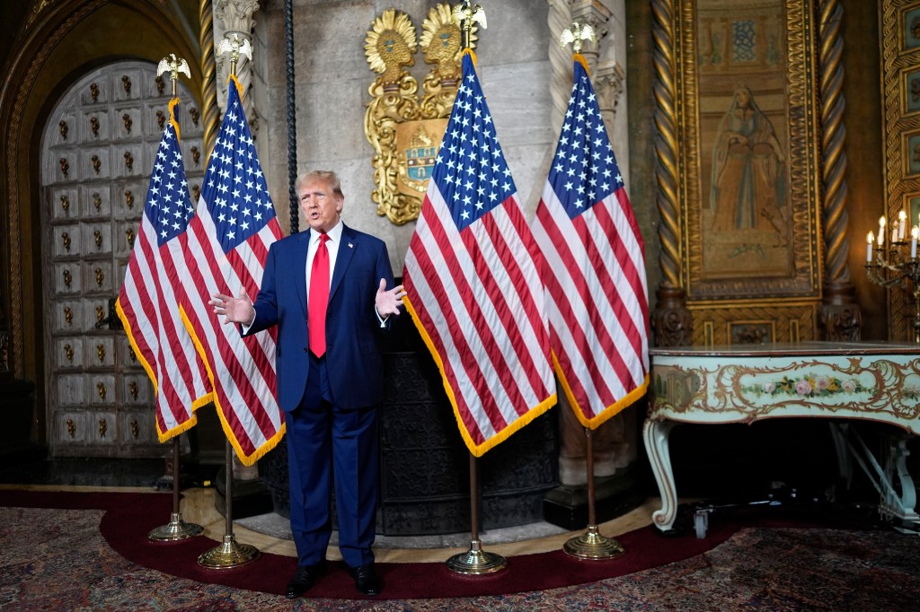 Donald Trump speaks at his Mar-a-Lago estate in Palm Beach, Florida, standing in front of multiple flags.