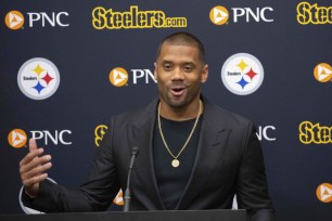 A man in a suit standing behind a microphone, presumably Russell Wilson, speaking at an NFL football news conference in Pittsburgh.