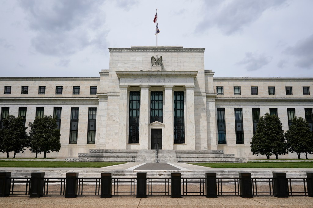 American flag flies above white building housing Federal Reserve with text on blue banner reading \"Federal Reserve Cautious Comments\".