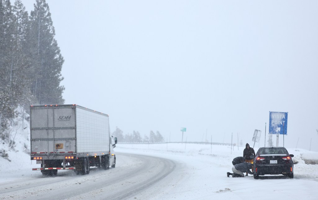 People check on tire chains as snow falls along Interstate 80 (I-80) in the Sierra Nevada mountains at the start of a powerful winter storm on February 29, 2024 near Soda Springs, California