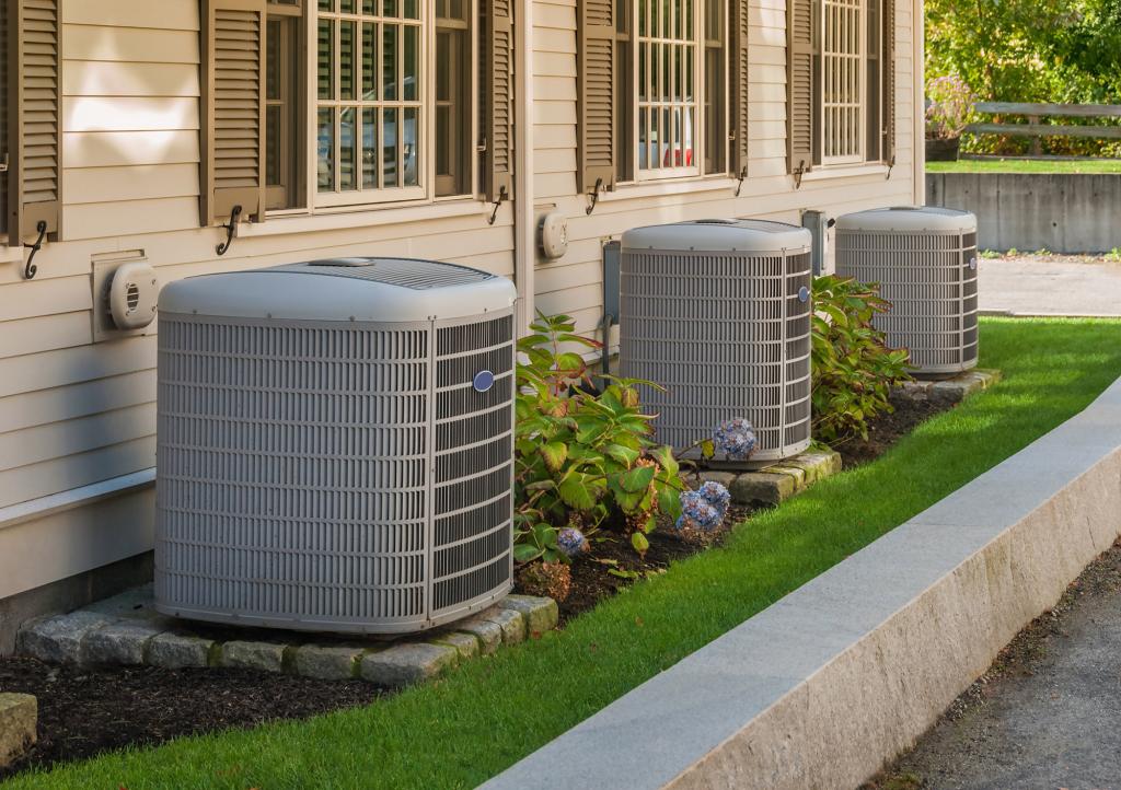 A row of air conditioning and heating units outside a condo building