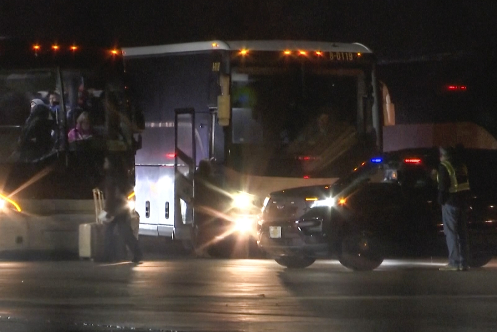 Migrants board buses at the airport at night