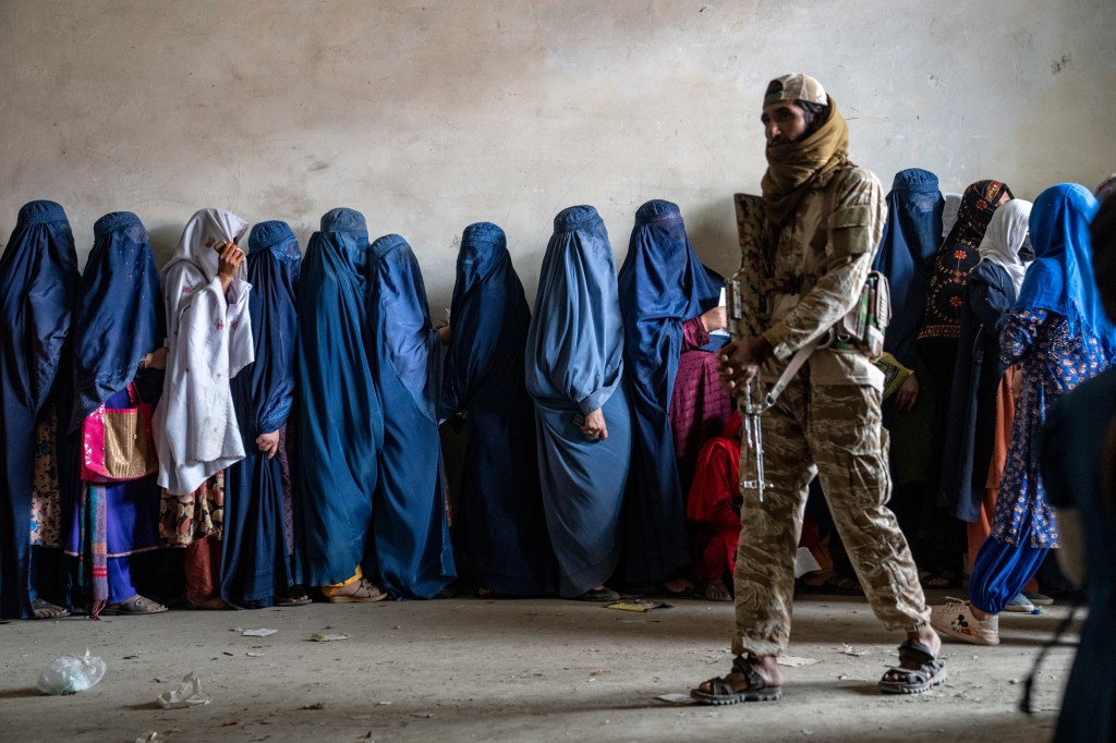 A Taliban fighter stands guard as women wait to receive food