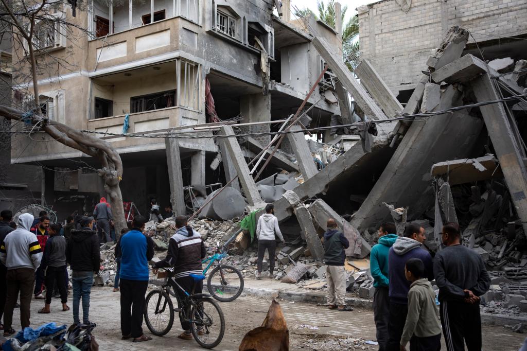 A group of people standing in front of a destroyed building in Israel-Palestine conflict