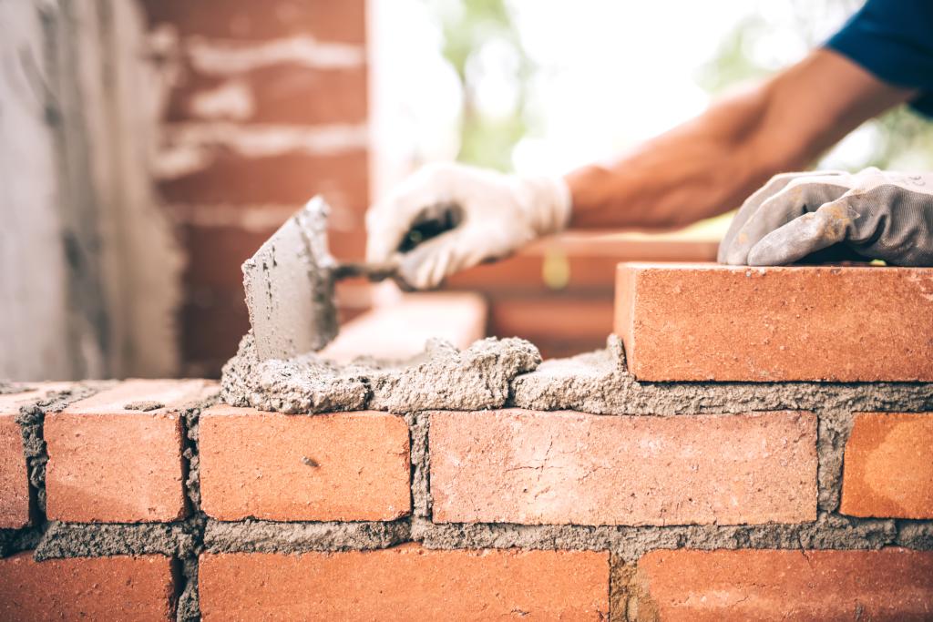 Bricklayer worker installing brick masonry on exterior wall with trowel putty knife