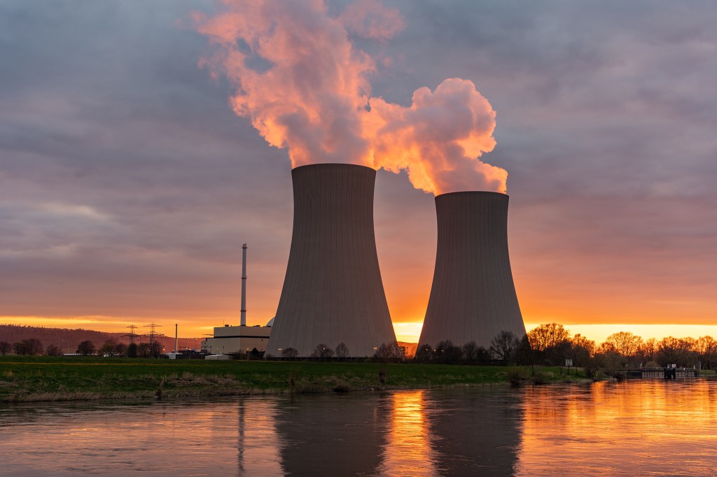 Nuclear power plant against sky by the river at sunset.