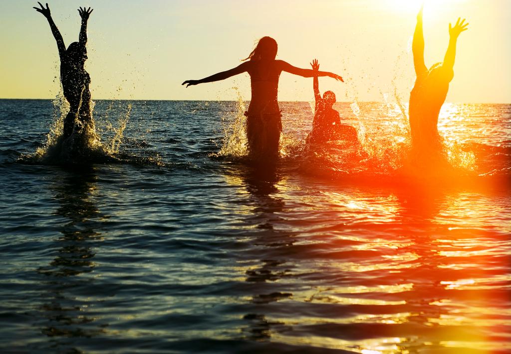 Silhouettes of young group of people jumping in ocean at sunset