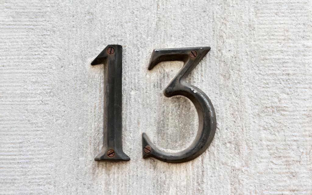 Closeup image of an old rusted metal number 13 on a gray wall