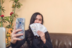 A woman taking a selfie while showing off a handful of cash.