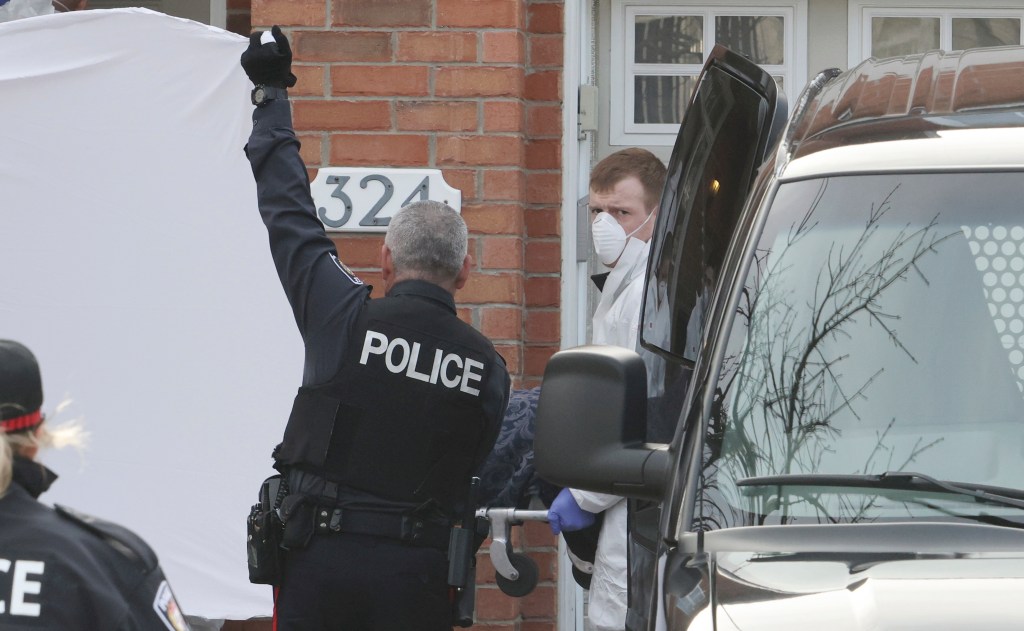 Police officers hold up a sheet as members of the coroner's office remove a body at the scene.