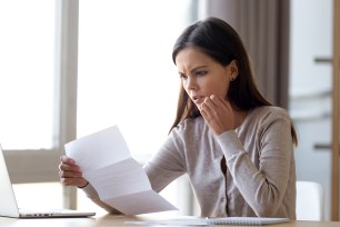 Disappointed young woman sit on table at home read bad news eviction notice in paperwork letter, shocked female surprised by unpleasant message warning notification received in paper mail