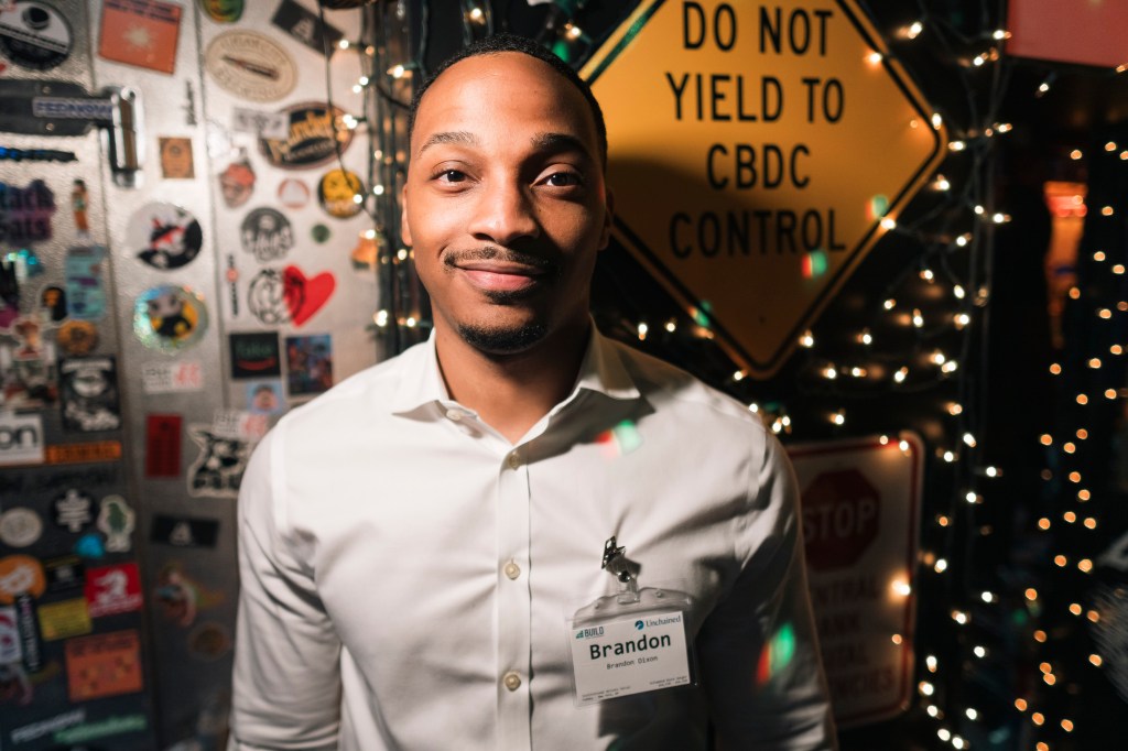 A man in a white shirt standing in a Bitcoin bar holding a drink. Photo taken by Stefano Giovannini at Greenwich Village Manhattan.