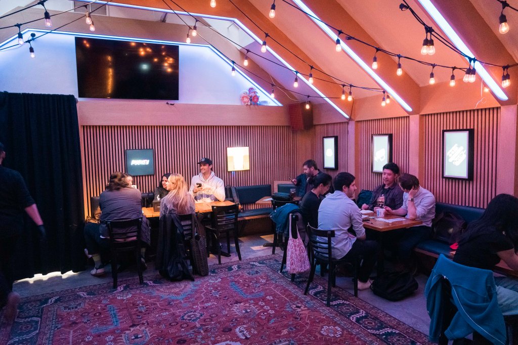 A crowded Bitcoin bar in Manhattan with people sitting at tables in a room with lights - photo by Stefano Giovannini.