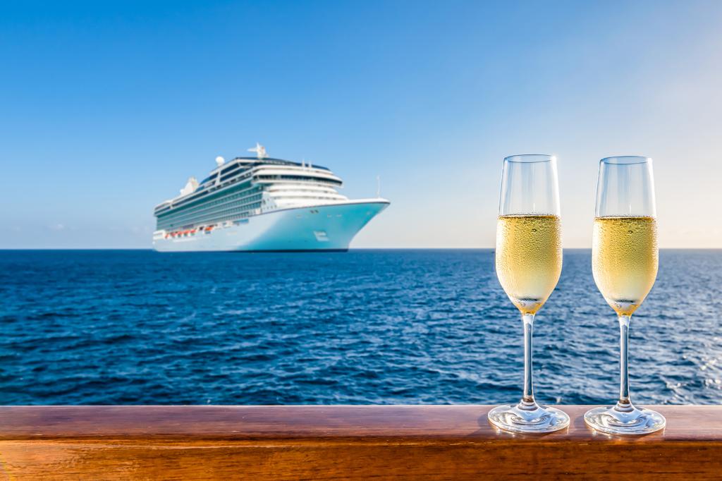 Two glasses of champagne placed on a railing overlooking a cruise ship at sunset