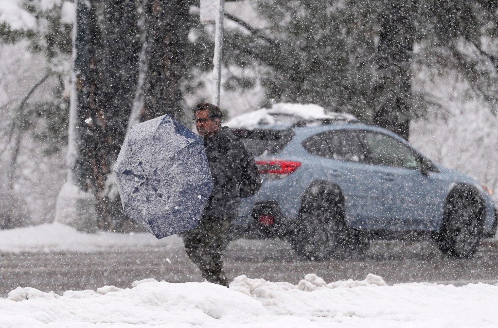 A pedestrian tries to clean off his umbrella while waiting for a bus at a stop along eastbound Speer Boulevard during the snowstorm in Denver in March 14, 2024. 