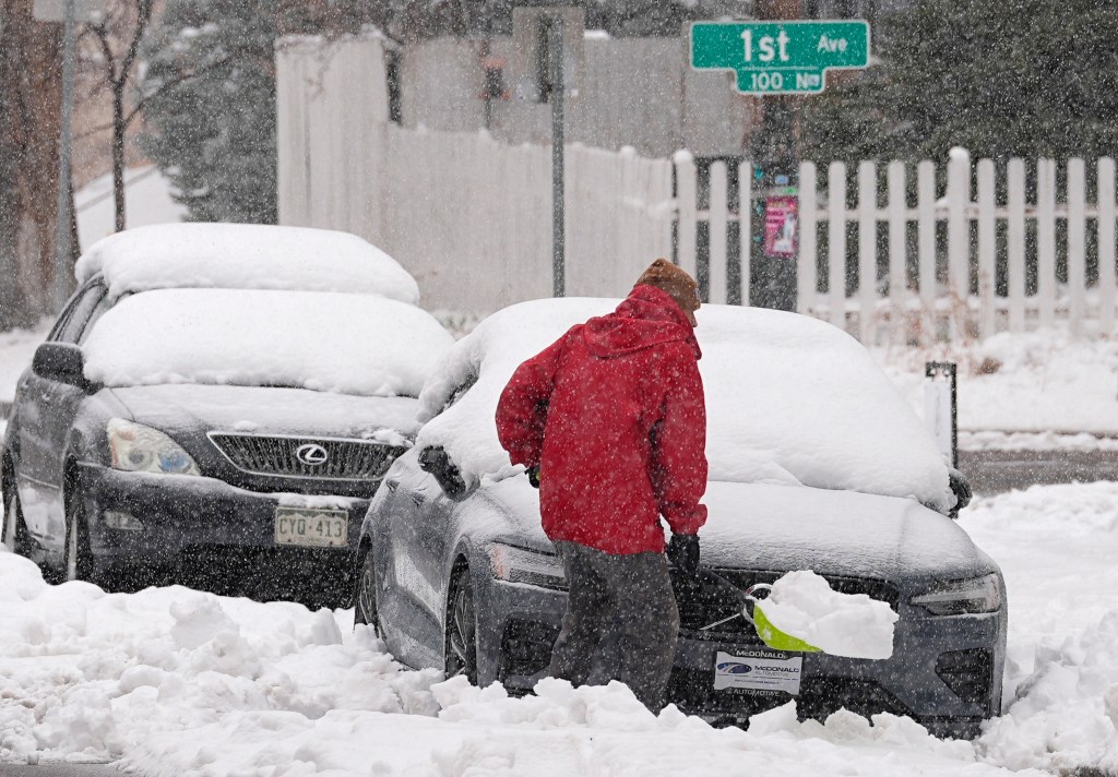 A person struggles to clear snow from in front of a vehicle parked along Washington Street as a late winter storm regained force late on March 14, 2024, in Denver. 