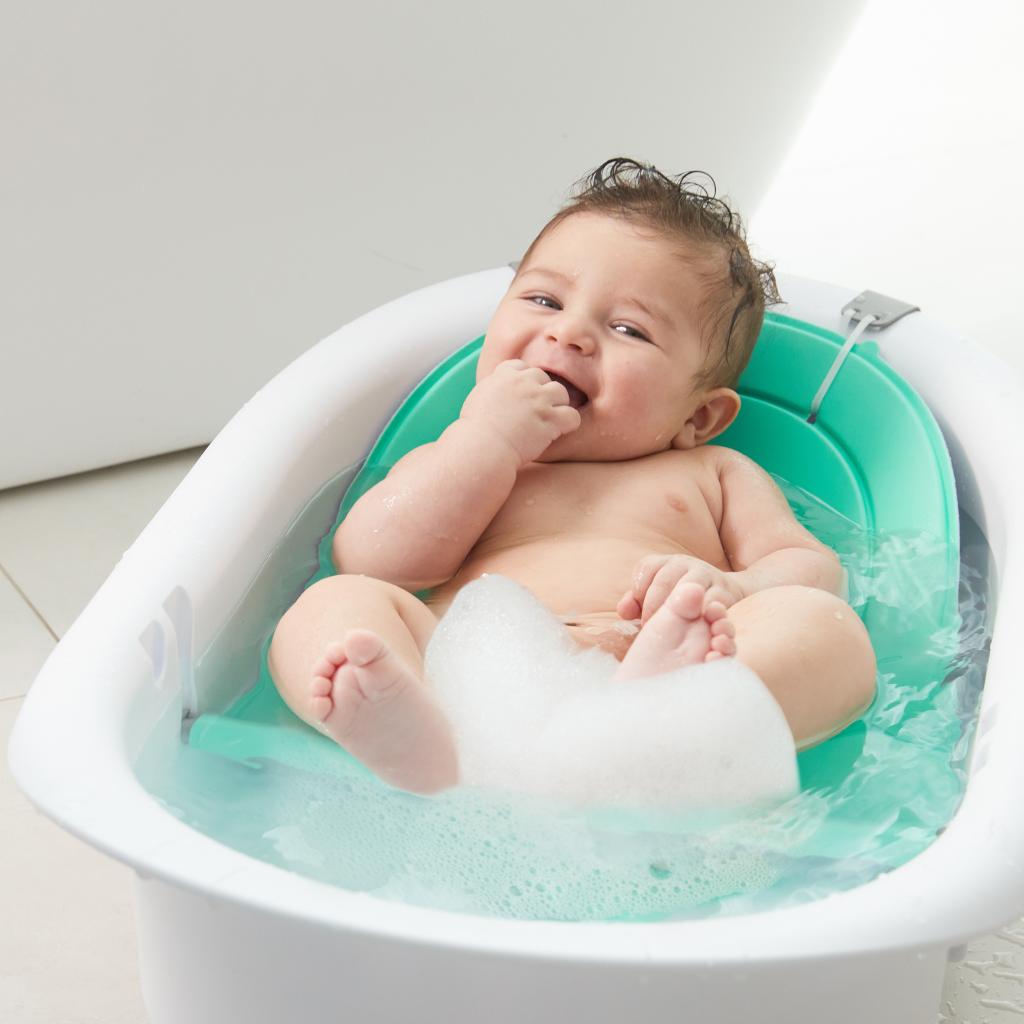 A baby sitting in a Frida Baby Bath tub with adjustable sling feature for safe bathing.