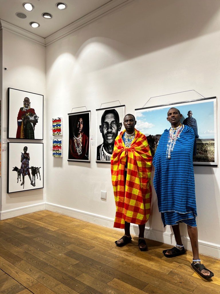 Two men standing in a room with pictures on the wall at the Oculus Humanculture Exhibit on March 29