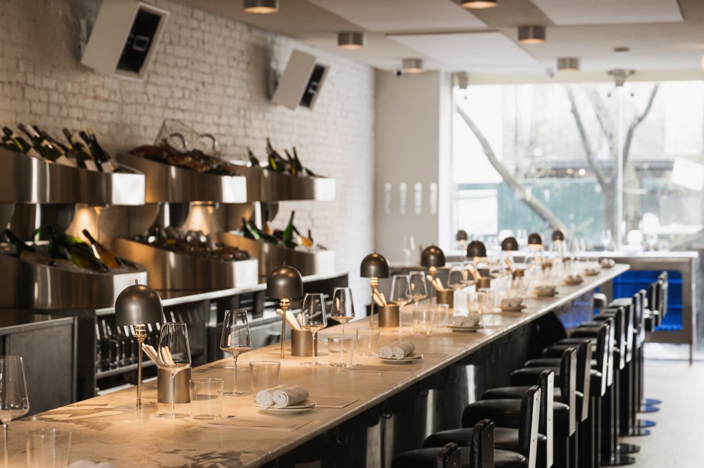 A long table with wine glasses and a group of chairs in the front bar section of Penny Interior