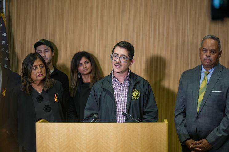 Travis County District Attorney Jose Garza speaking at a press conference with a group of people standing behind him in a room.