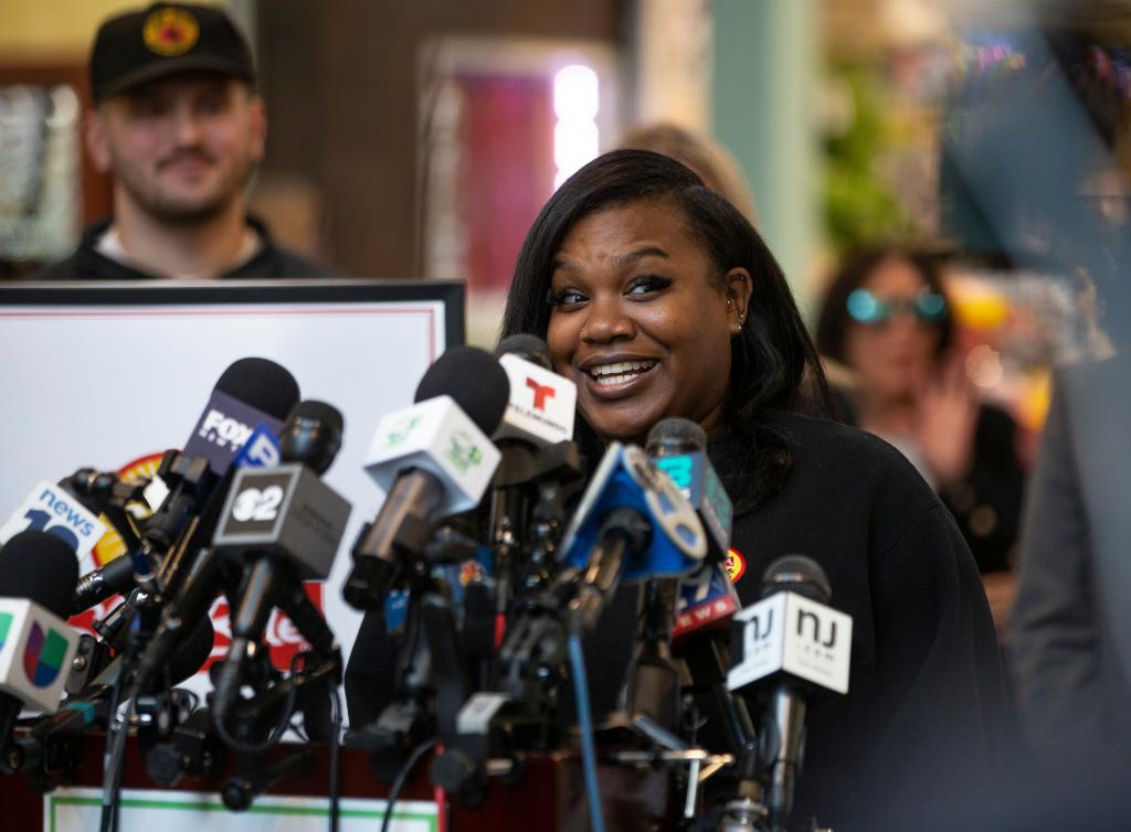 Tiyahna Bambaata, a woman smiling at a microphone, after selling the winning lottery ticket at a ShopRite Liquor store in Neptune, New Jersey