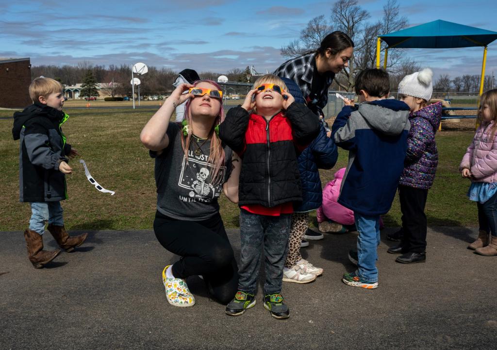 A child and a young woman look up at the sky wearing eclipse glasses.