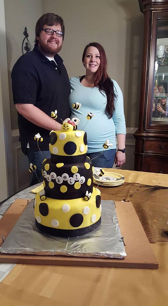 Joshua Bowling and a pregnant Annica stand behind.a cake and smile