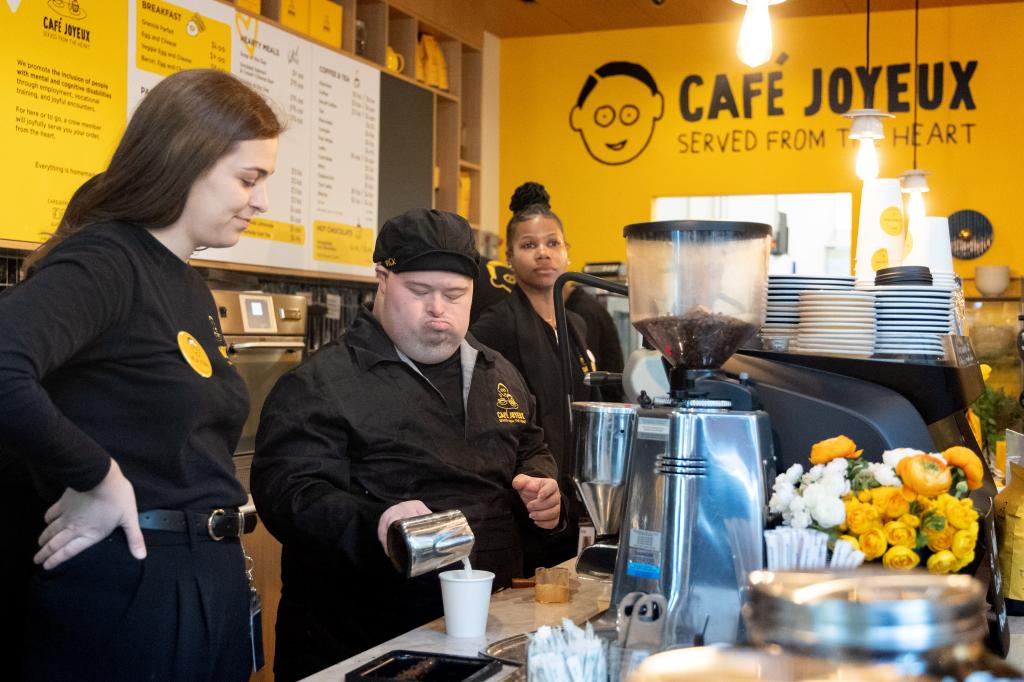 Assistant manager and head trainer Sarah Parkes oversees crew member Nick Stanford pouring heated milk into a coffee while behind the counter