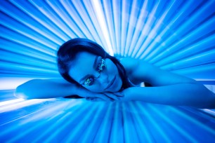 Attractive young woman smiling while tanning in solarium.
