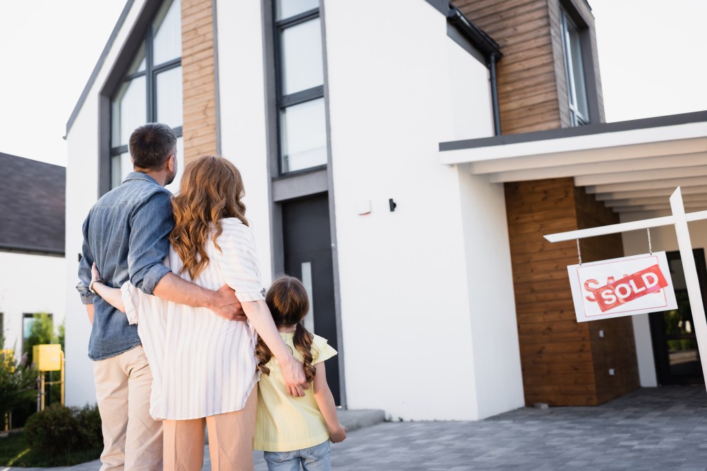 Back view of a family standing near a 'Sold' sign in front of a house