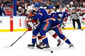 Noah Dobson and Adam Pelech of New York Islanders compete for the puck with Jack Hughes of New Jersey Devils.