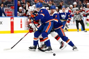 Noah Dobson and Adam Pelech of New York Islanders compete for the puck with Jack Hughes of New Jersey Devils.