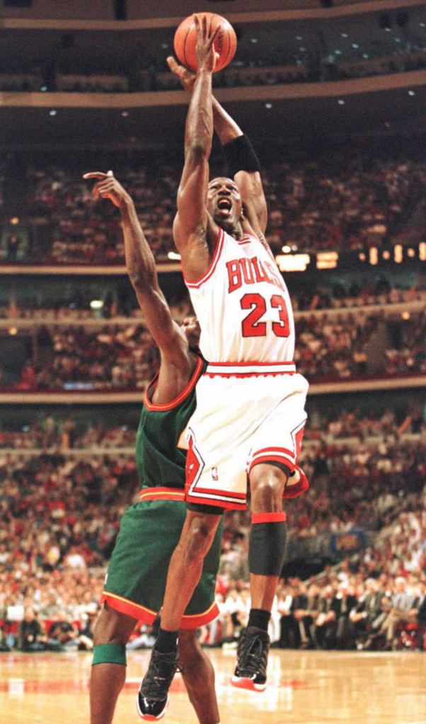 Chicago Bulls' Michael Jordan in white jersey grabbing a rebound from Shawn Kemp of the Seattle SuperSonics during game six of the NBA Finals