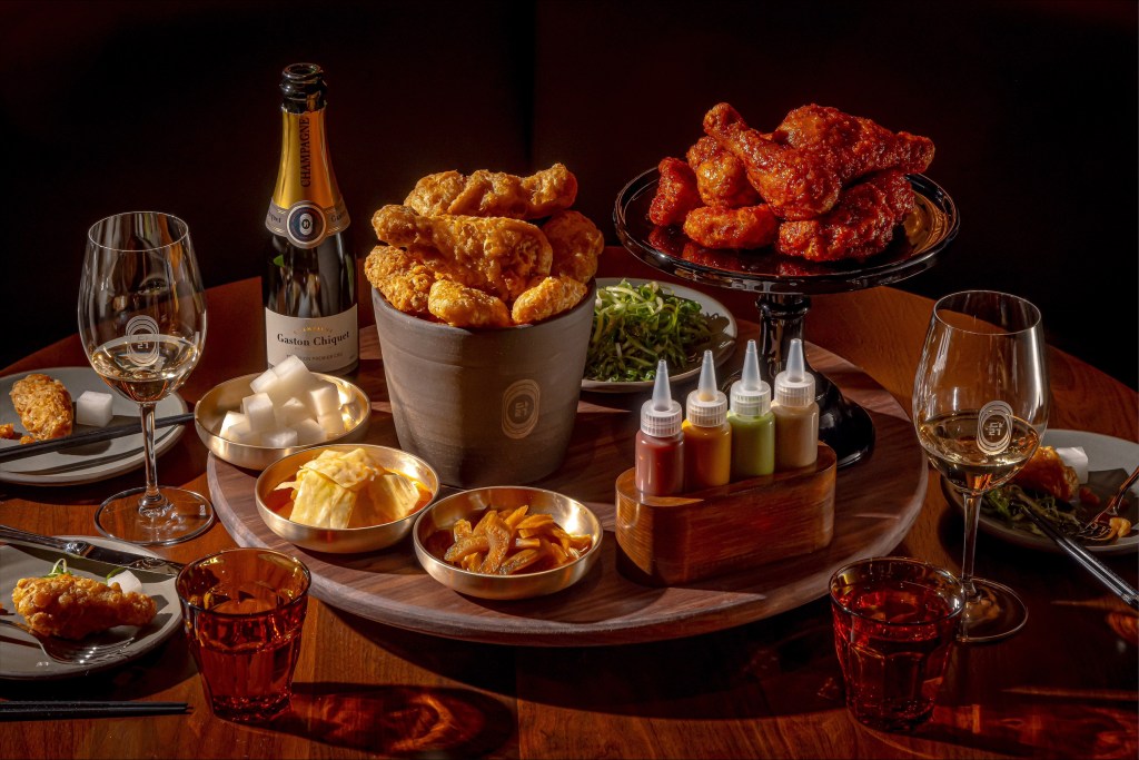 A tray of various foods included in the restaurant's Bucket List prix fixe, featuring chicken consommé, pickled vegetables, salads, two styles of fried chicken with dipping sauces, chilled noodles and frozen yogurt.