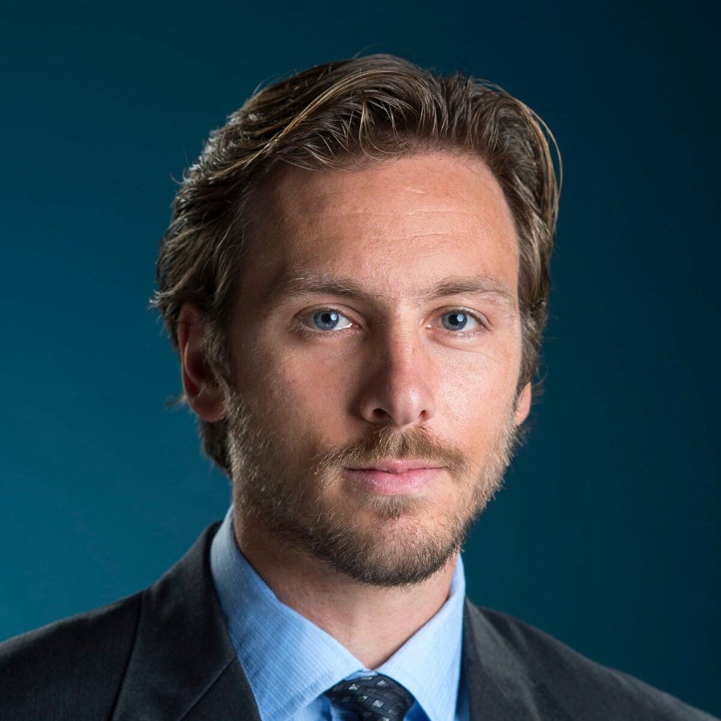 A photo of Andrew Lohn in a suit looking at the camera.