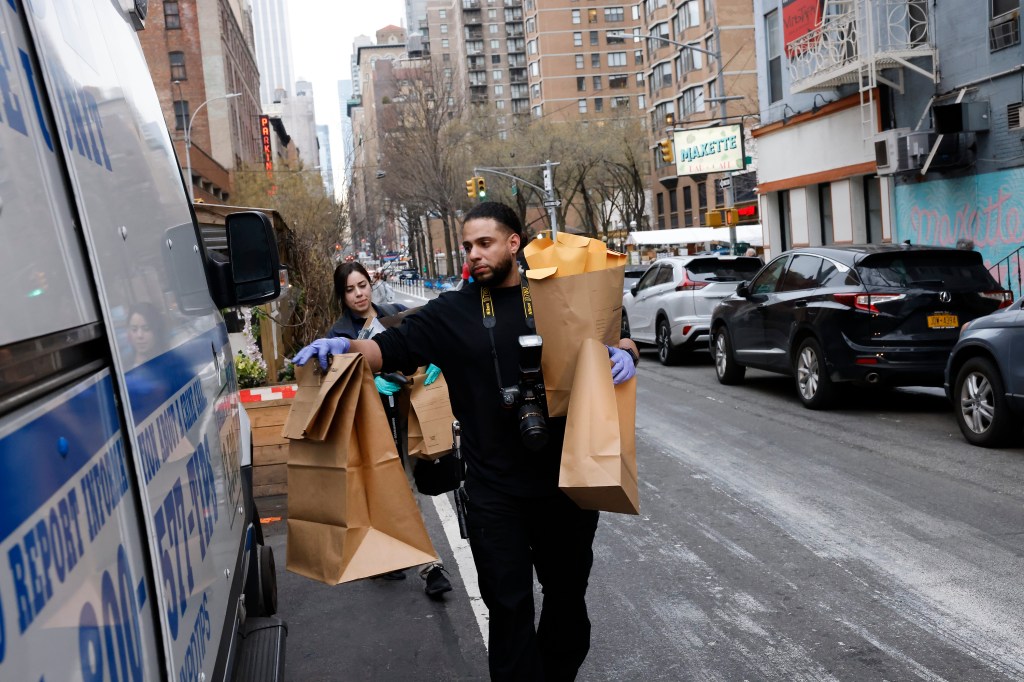 A male and female investigator load brown paper bags of evidence into an NYPD van.