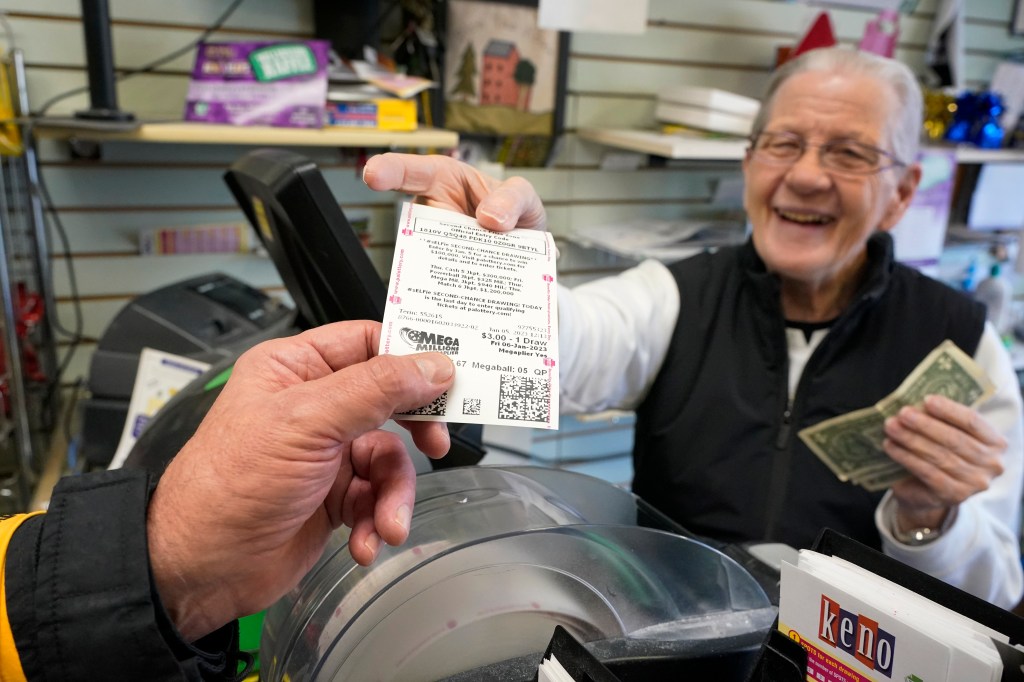 A Pennsylvania store owner hands a customer a Mega Millions lottery ticket on Jan. 5, 2022, in Mt. Lebanon, Pa.