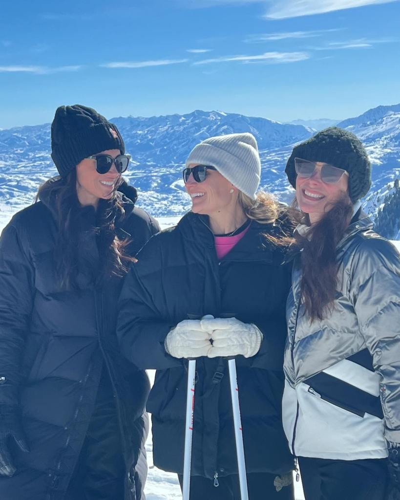 A group of three women, including Meghan Markle, wearing ski gear and posing on a snow-covered mountain.