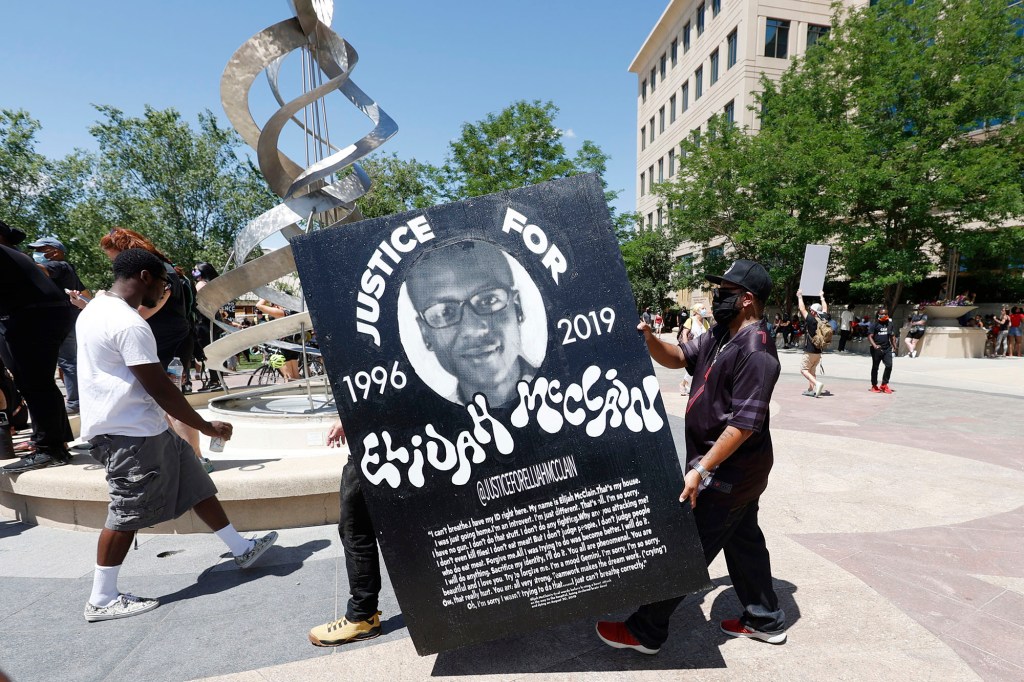 Demonstrators carrying a large placard with a picture of Elijah McClain wearing a black hat during a rally and march outside a police department.