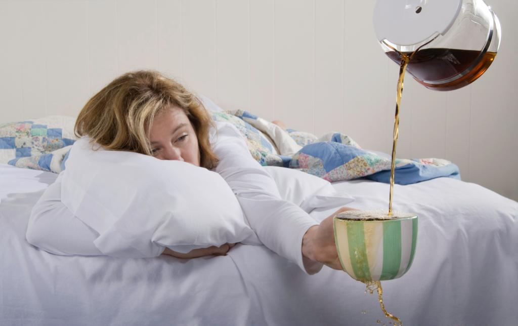 Exhausted woman in bed wanting more coffee.