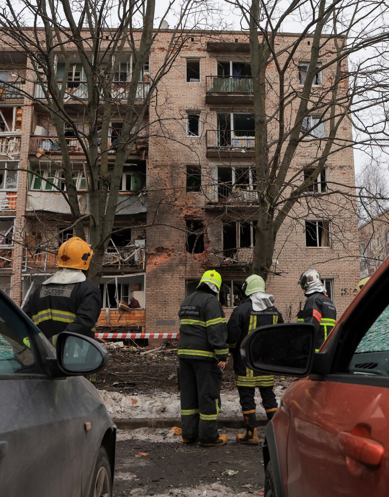 Firefighters gather outside a damaged and charred building following an alleged drone attack. 