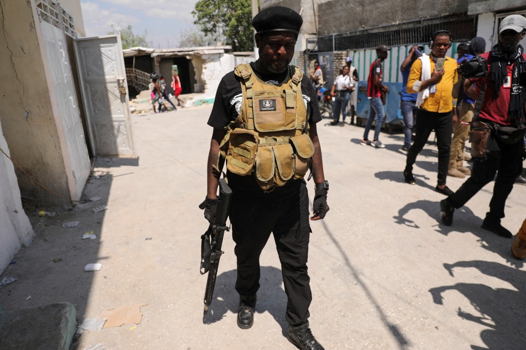 Former police officer Jimmy "Barbecue" Cherizier, leader of an alliance of armed groups, holding a gun, surrounded by journalists in Port-au-Prince.