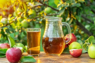 Fresh apple juice and organic apples on wooden table. Summer orchard in the evening sun rays at the background.