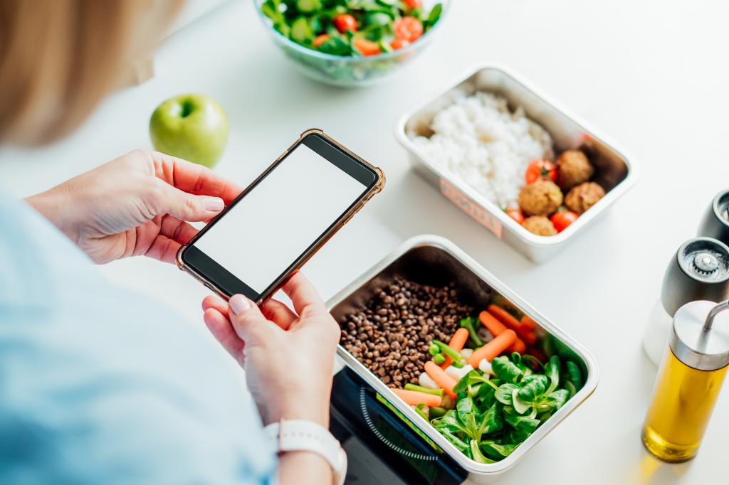 Healthy diet meal prep on a kitchen scale. Woman holding phone with blank screen. Weight loss, balanced portion.