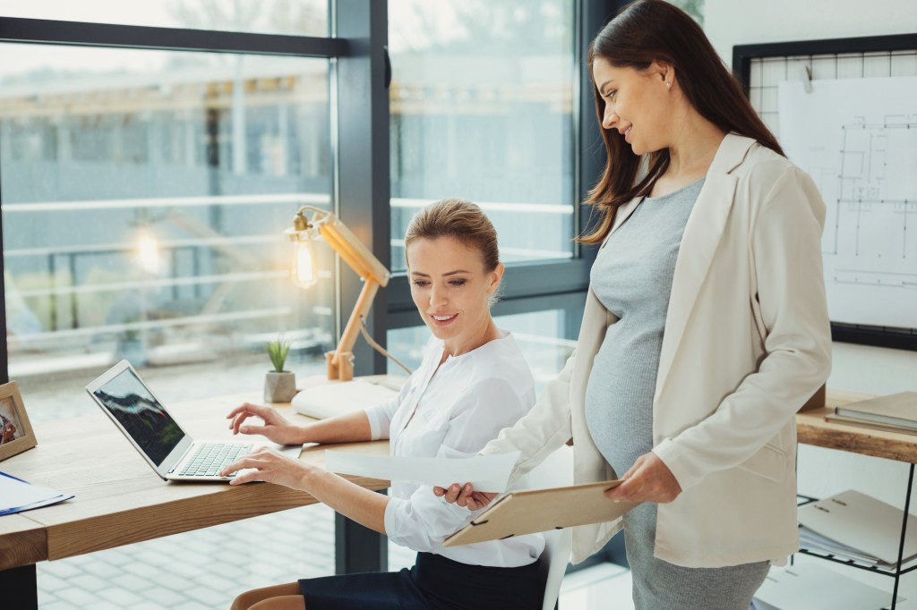 Pregnant woman standing speaking to a seated woman in an office
