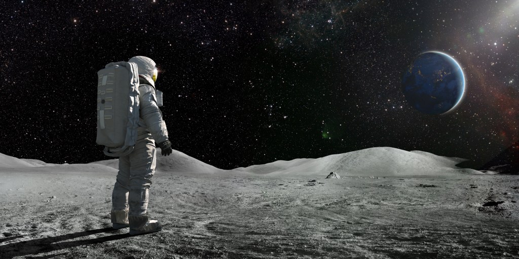 A lone astronaut standing facing away from the camera dressed in full space suit with backpack.