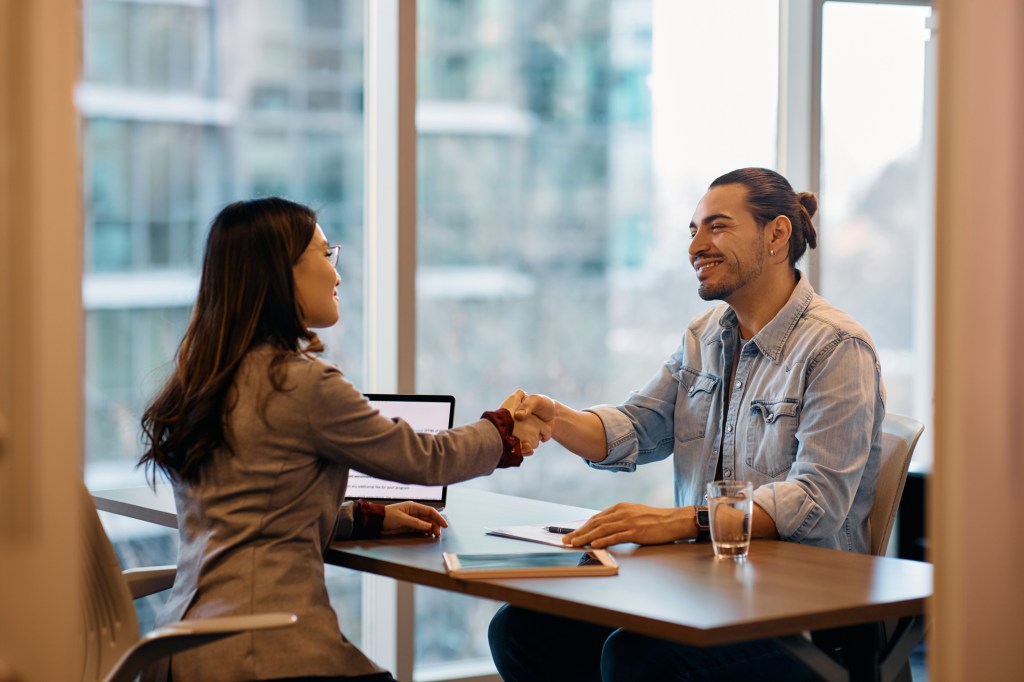 Human resource manager shaking hands with male candidate during job interview in the office.