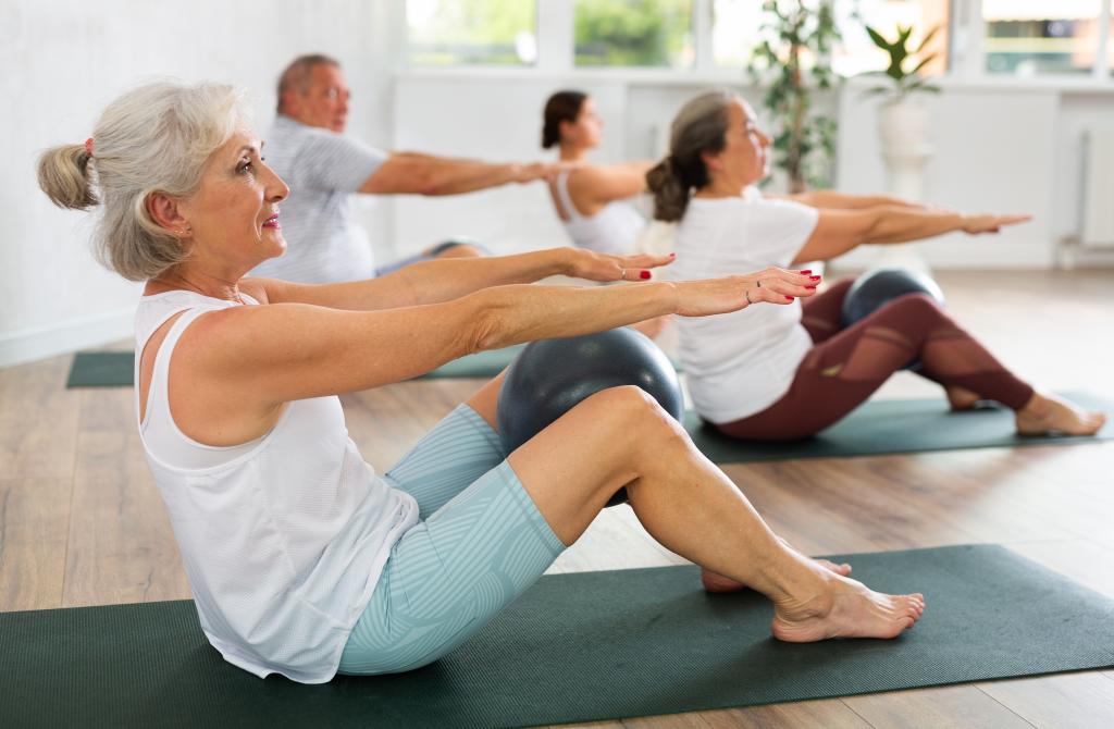 Portrait of mature people doing exercises for press with pilates ball during group class in fitness studio.