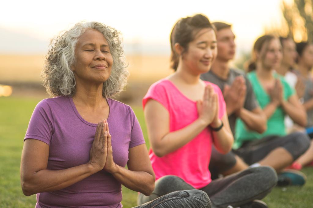 A senior woman of Pacific Islander descent meditates during a group yoga class.